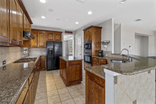 Kitchen featuring black appliances, light tile patterned flooring, ventilation hood, dark stone countertops, and backsplash | Image 11