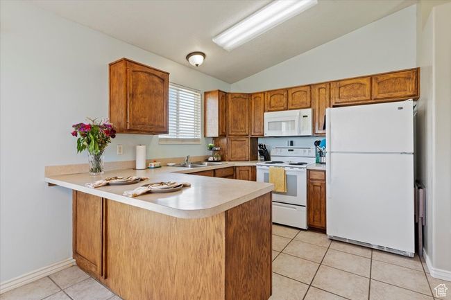 Kitchen with white appliances, a peninsula, a chandelier, vaulted ceiling, and light countertops | Image 10