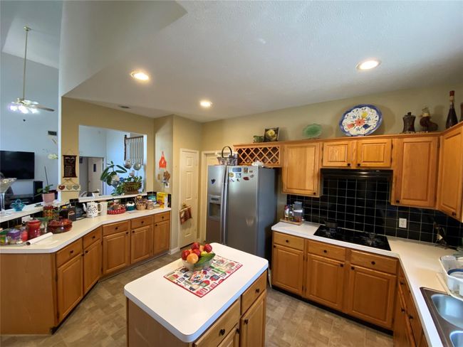 Kitchen with black gas cooktop, backsplash, stainless steel fridge, decorative light fixtures, and a kitchen island | Image 23