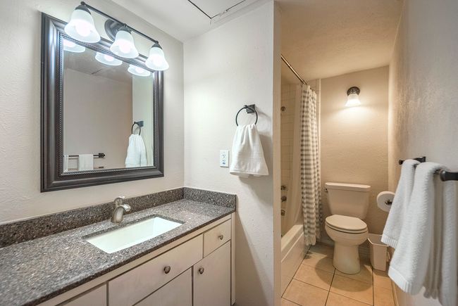 A minimalist wet room layout showcasing a vanity unit with stylish lighted mirror on the wall, towel racks, a bathtub and a toilet. | Image 16