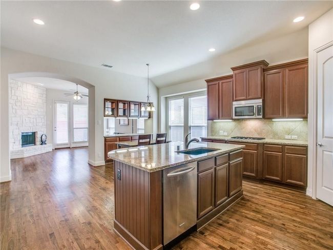 Kitchen featuring appliances with stainless steel finishes, a sink, dark wood-type flooring, tasteful backsplash, and light stone countertops | Image 7