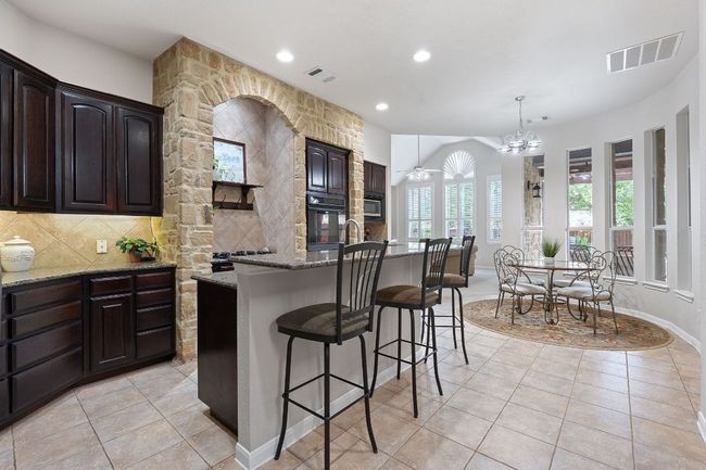 Kitchen with black oven, light stone counters, light tile patterned flooring, a breakfast bar area, and decorative backsplash | Image 6