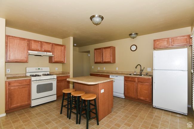 Kitchen featuring light countertops, white appliances, under cabinet range hood, a sink, and a center island | Image 12