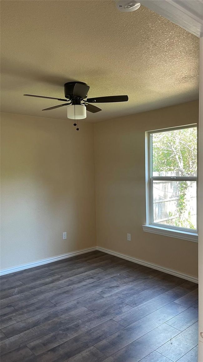 Empty room with dark wood-style floors, a textured ceiling, baseboards, and ceiling fan | Image 4