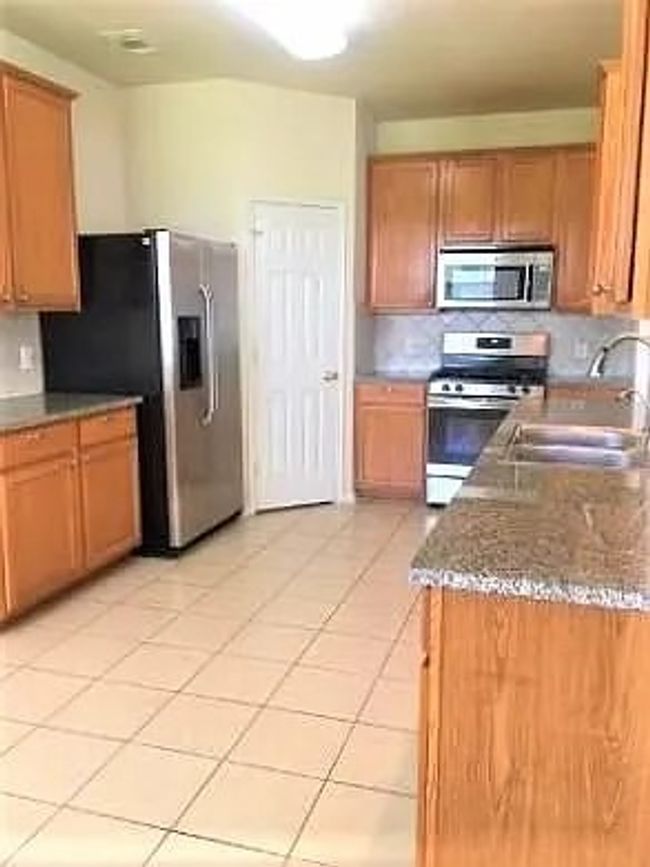 Kitchen featuring appliances with stainless steel finishes, a sink, light tile patterned floors, stone countertops, and brown cabinetry | Image 11