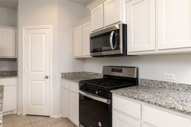 Kitchen featuring stainless steel appliances, white cabinetry, light stone counters, and light tile patterned floors | Image 8