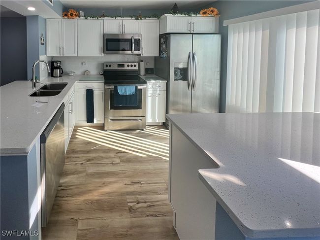 Kitchen with appliances with stainless steel finishes, white cabinetry, sink, and light stone counters | Image 4