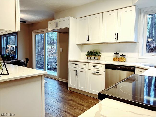 Kitchen featuring stainless steel dishwasher, light stone counters, white cabinets, backsplash, and light wood-type flooring | Image 5