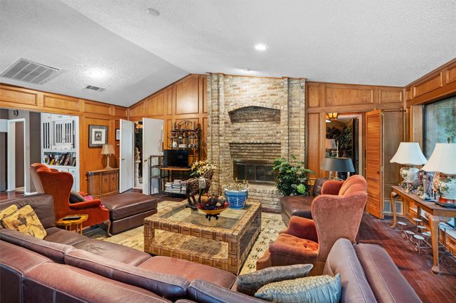 Living area featuring wood finished floors, a textured ceiling, wooden walls, lofted ceiling, and visible vents | Image 5