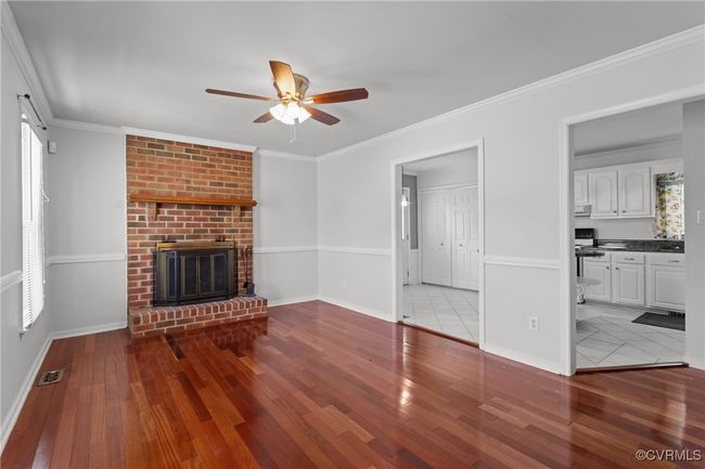 Unfurnished living room featuring baseboards, visible vents, a brick fireplace, ceiling fan, and hardwood / wood-style flooring | Image 7