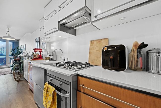 Kitchen with white cabinets, light countertops, hardwood / wood-style flooring, under cabinet range hood, and stainless steel gas stovetop | Image 9