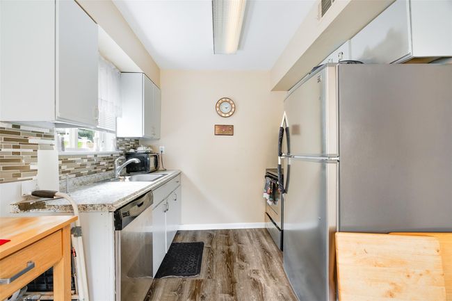 Kitchen with appliances with stainless steel finishes, light countertops, dark wood-style floors, white cabinets, and backsplash | Image 10