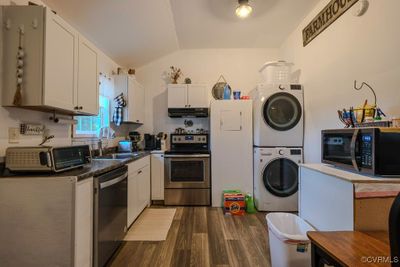 Kitchen with stacked washing maching and dryer, stainless steel appliances, sink, white cabinetry, and lofted ceiling | Image 3