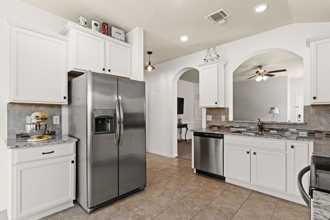 Kitchen with arched walkways, appliances with stainless steel finishes, a ceiling fan, white cabinetry, and light stone countertops | Image 10