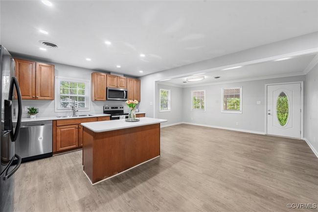 Kitchen with stainless steel appliances, light countertops, a kitchen island, light wood-type flooring, and ornamental molding | Image 11