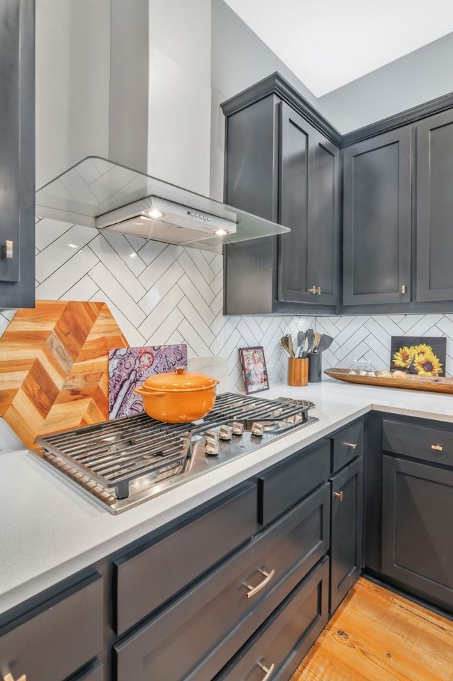 Kitchen with wall chimney range hood, light countertops, backsplash, and stainless steel gas cooktop | Image 11