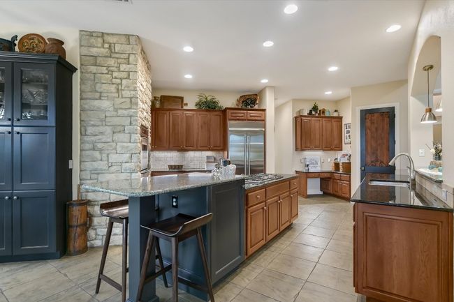 Kitchen with stainless steel appliances, dark stone countertops, a breakfast bar area, planning corner, pantry with iron trimmed door. | Image 10