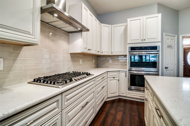 Kitchen with backsplash, wall chimney exhaust hood, dark wood-style flooring, appliances with stainless steel finishes, and light stone counters | Image 4