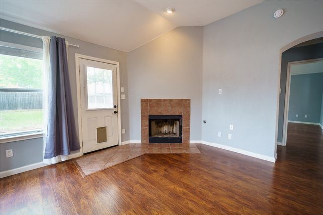 Living room featuring wood finished floors, lofted ceiling, arched walkways, a tile fireplace, and baseboards | Image 9