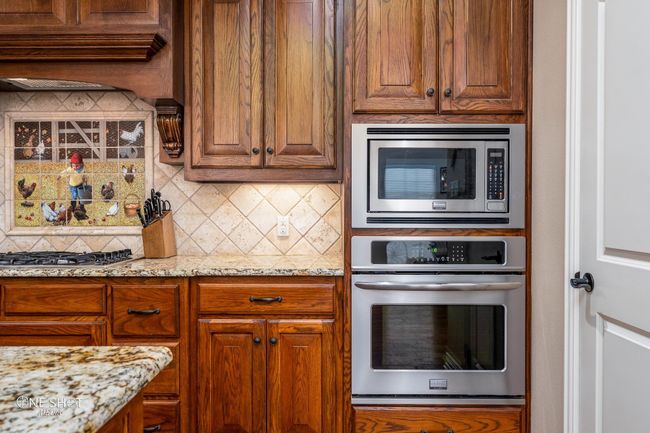 Kitchen with stainless steel appliances, decorative backsplash, light stone counters, and brown cabinets | Image 15