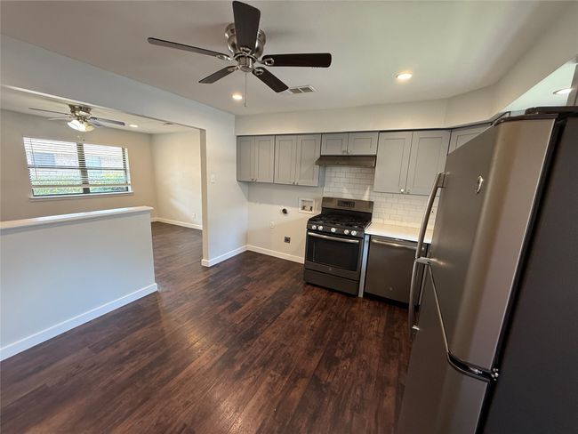 Kitchen featuring stainless steel appliances, gray cabinetry, a ceiling fan, decorative backsplash, and dark wood finished floors | Image 6