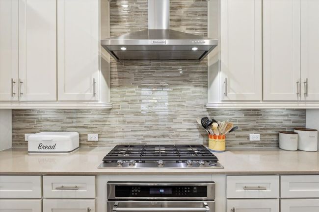 Kitchen with wall chimney exhaust hood, oven, stainless steel gas stovetop, and light quartz countertops | Image 14