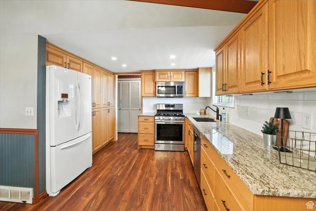 Kitchen with stainless steel appliances, dark wood-style flooring, light stone counters, tasteful backsplash, and recessed lighting | Image 10