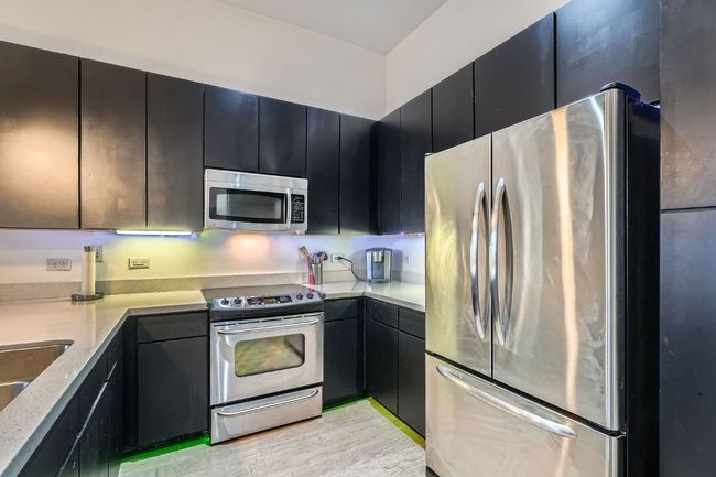 Kitchen featuring light stone countertops, dark cabinetry, appliances with stainless steel finishes, and light wood-style floors | Image 10