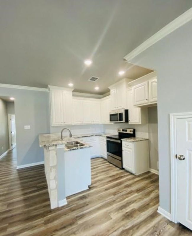 Kitchen with appliances with stainless steel finishes, white cabinets, wood finished floors, ornamental molding, and baseboards | Image 4