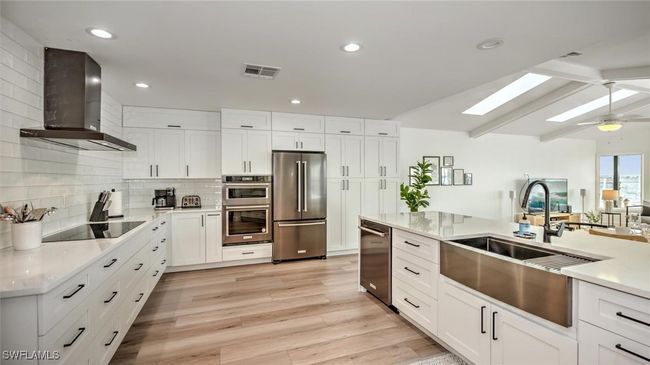 Kitchen featuring stainless steel appliances, wall chimney exhaust hood, a skylight, decorative backsplash, and light countertops | Image 16