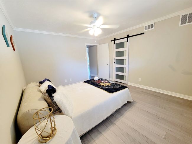 Bedroom featuring ceiling fan, a barn door, ornamental molding, and light hardwood / wood-style flooring | Image 10