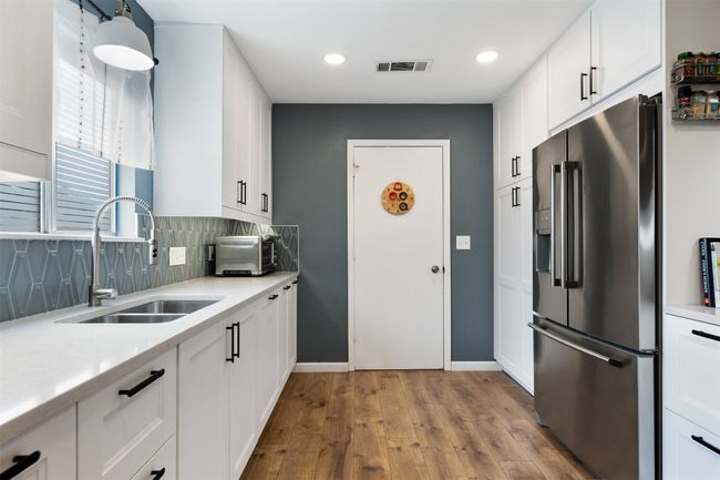 Kitchen with hardwood / wood-style floors, stainless steel fridge with ice dispenser, visible vents, a sink, and tasteful backsplash | Image 14