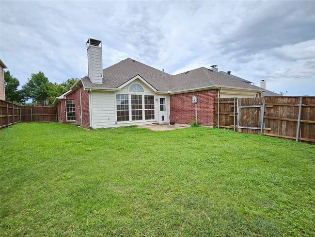 Rear view of property featuring brick siding, a fenced backyard, a chimney, and roof with shingles | Image 30