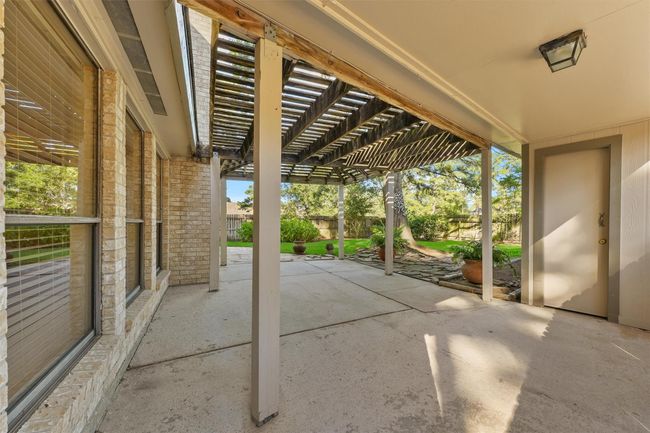This photo showcases a covered patio area with a pergola, providing partial shade and an open view to a lush backyard. The space is ideal for outdoor relaxation and entertaining. | Image 21