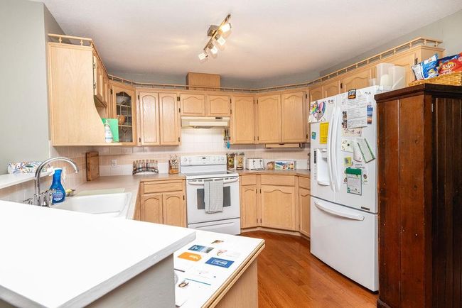 Kitchen featuring white appliances, a sink, light brown cabinetry, under cabinet range hood, and backsplash | Image 9