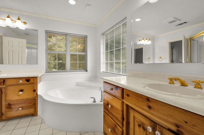 Bathroom with ornamental molding, two vanities, tile patterned flooring, a garden tub, and a shower with shower door | Image 16