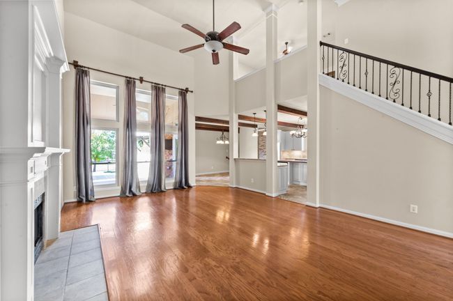 Unfurnished living room featuring a ceiling fan, a tile fireplace, a high ceiling, wood finished floors, and a chandelier | Image 14
