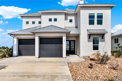 This is a modern two-story home features a light gray exterior with white trim and a dark gray roof. It includes a two-car garage, a covered entrance, and a low-maintenance landscaped front yard. | Image 1