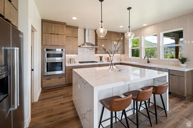 Kitchen with stainless steel appliances, wall chimney range hood, a sink, dark wood finished floors, and a kitchen island | Image 12