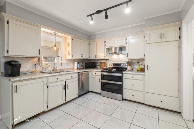 Kitchen with decorative backsplash, cream cabinets, a sink, stainless steel appliances, and wall chimney exhaust hood | Image 10
