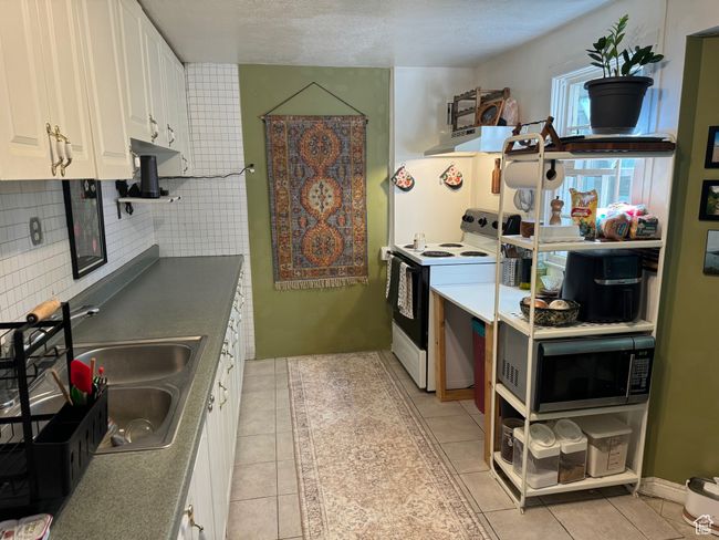 Kitchen featuring a sink, stainless steel microwave, white cabinetry, white range with electric stovetop, and light tile patterned floors | Image 20