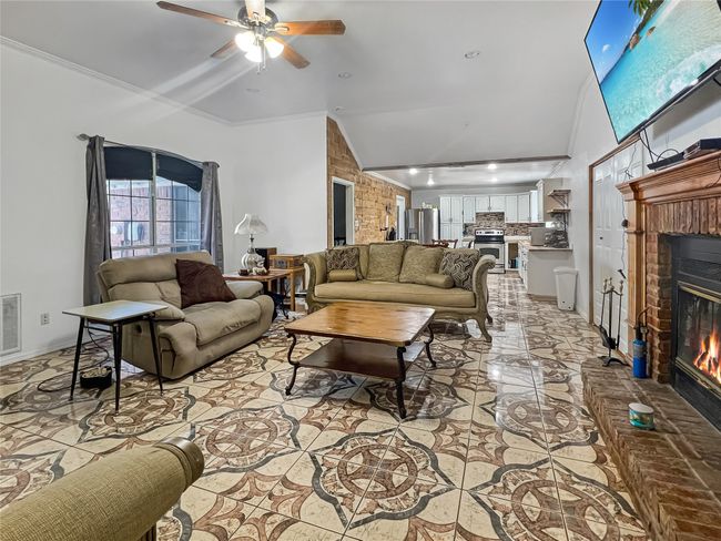 Living area with a brick fireplace, vaulted ceiling, ceiling fan, light tile patterned floors, and crown molding | Image 14