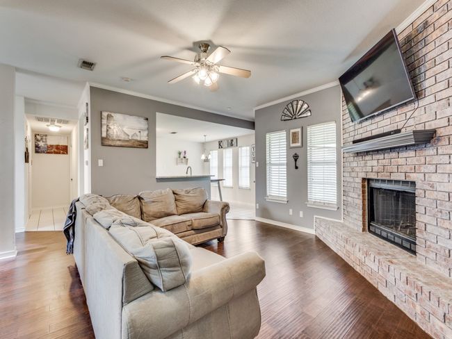 Living room with a ceiling fan, crown molding, wood finished floors, a fireplace, and baseboards | Image 10