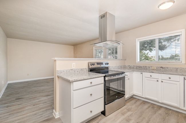 Kitchen with stainless steel range with electric cooktop, white cabinets, a peninsula, island range hood, and healthy amount of natural light | Image 13