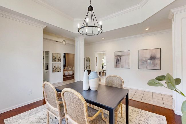 Dining area featuring ornate columns, a tray ceiling, wood finished floors, a chandelier, and ornamental molding | Image 15