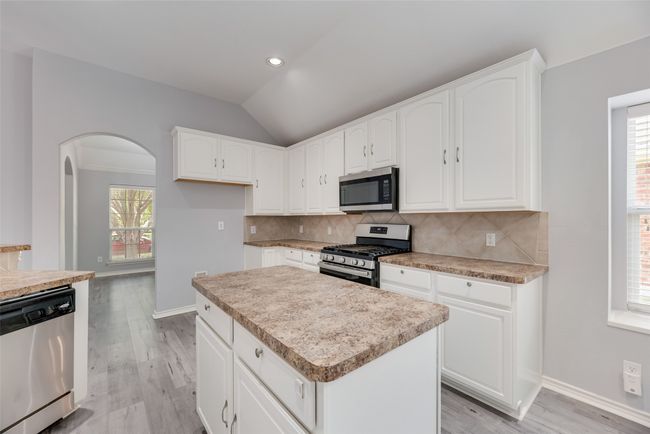Kitchen featuring appliances with stainless steel finishes, light wood-style floors, tasteful backsplash, baseboards, and a center island | Image 7