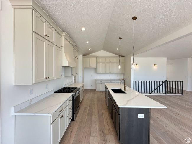 Kitchen with stainless steel gas stove, light wood-style floors, a kitchen island with sink, lofted ceiling, and light stone counters | Image 9