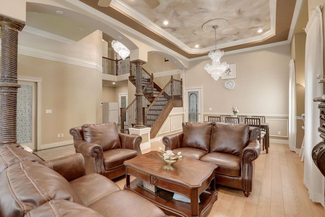 Living room featuring arched walkways, decorative columns, stairway, a notable chandelier, and a tray ceiling | Image 10