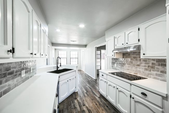 Kitchen with dark wood-type flooring, under cabinet range hood, white cabinets, black electric cooktop, and a sink | Image 6