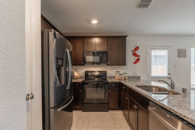 Kitchen featuring visible vents, light tile patterned floors, a sink, black appliances, and light stone countertops | Image 4
